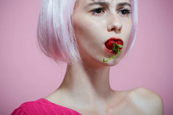 Γυναίκα σε ροζ περούκα μαλλιά κρατήστε κόκκινη φράουλα στο στόμα — Φωτογραφία Αρχείου