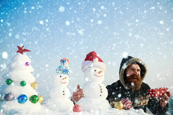 Mann lächelt mit Schneemännern und verschneitem Weihnachtsbaum — Stockfoto