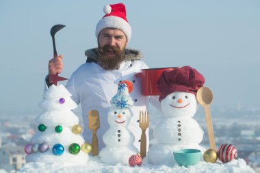 Mavi gökyüzü üzerinde mutlu aşçı, kardan adam ve kar xmas ağacı
