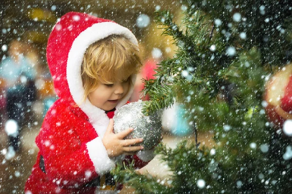 Child with silver ball on Christmas tree wearing santa costume — Stock Photo, Image