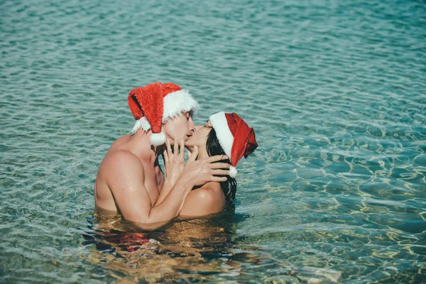 Різдвяна пара закоханий поцілунок як Санта в пляжній воді — стокове фото