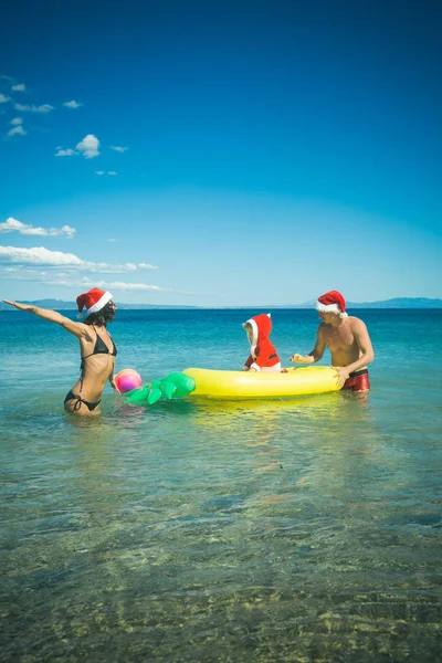 Weihnachtsfamilie mit Weihnachtsmütze am Strand mit Matratze — Stockfoto