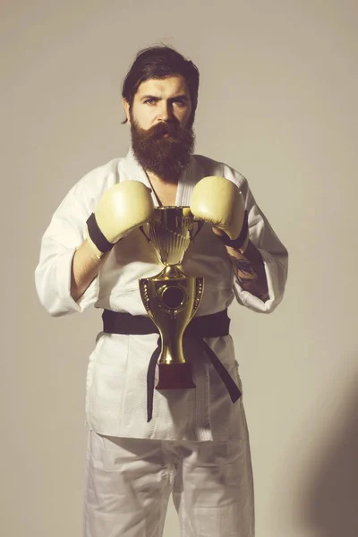 bearded karate man in kimono, boxing gloves, champion cup