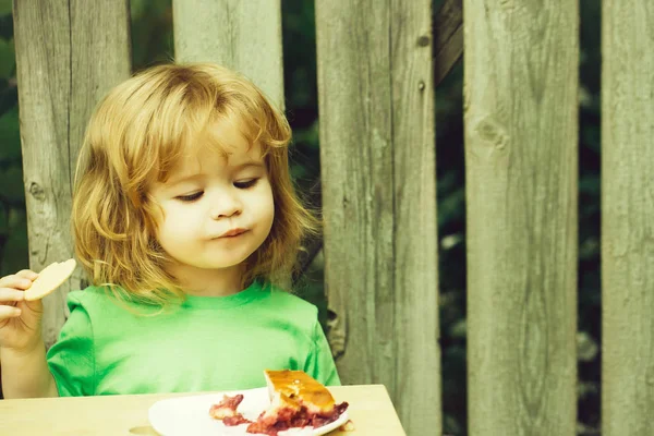 small boy eating pie near wooden fence