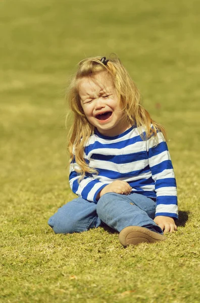 Malheureux bébé garçon mignon assis sur l'herbe verte dans le parc — Photo