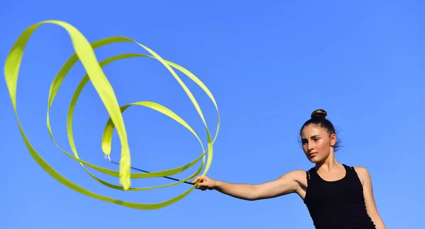 Woman gymnast swirl green ribbon on blue sky background