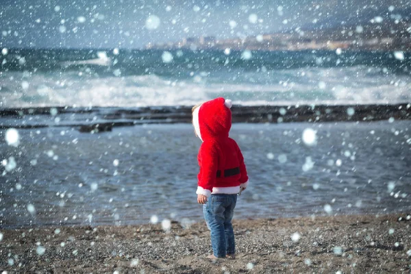 Santa baby i röd kostym gå barfota på stranden — Stockfoto