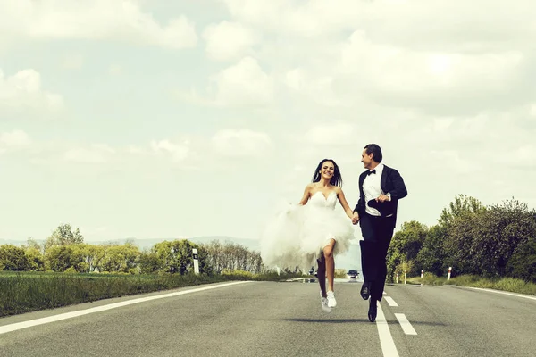 Casamento casal feliz correndo na estrada — Fotografia de Stock