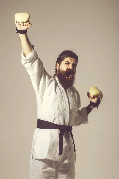 bearded shouting happy karate man in kimono and boxing gloves