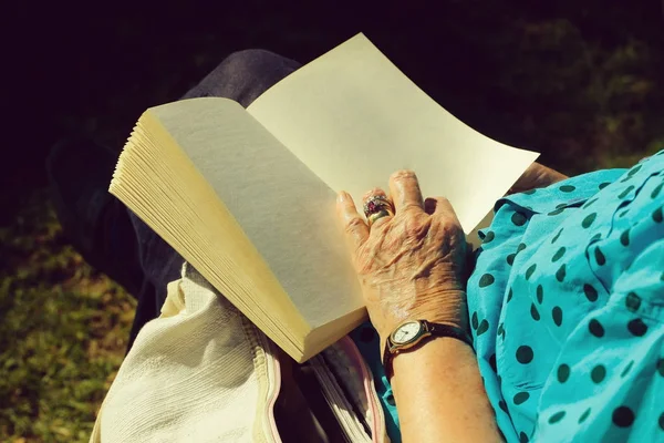 Kvinnlig hand med rynkig hud håller öppen bok — Stockfoto
