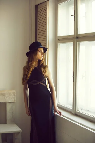 Красивая девушка в шляпе и платье на стул и окно — стоковое фото