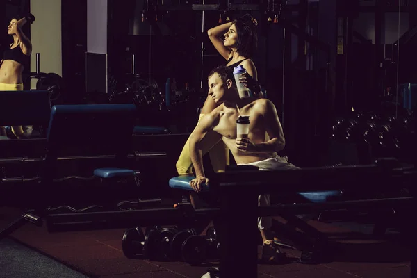 Hombre muscular y chica sexy en entrenador de gimnasio con botella — Foto de Stock