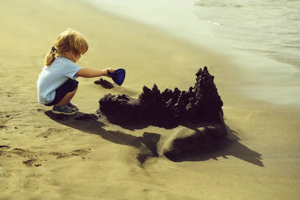 Lindo bebé niño construye castillo de arena en la playa del mar — Foto de Stock