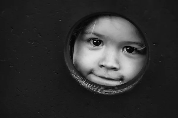 Милый веселый мальчик смотрит через круглую дыру в красной стене — стоковое фото