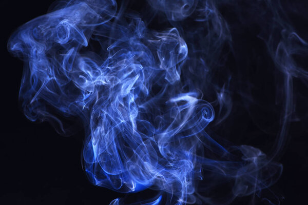 Blue ink in freeze motion, powder splatted explosion. Spirit and ghost, miracle. Blue smoke on black background. Smoking cloud backdrop. Abstract background with smoke.
