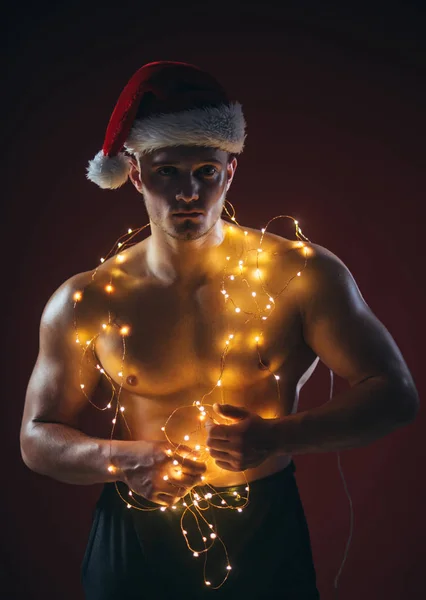 新年のストリップと大人のための贈り物 ガーランドで筋肉ボディを持つサンタ クリスマス パーティーとセックス ゲーム サンタ衣装の若い男は 女の子のため提示します クリスマスでセクシーなアスリートの男性や少年を呼び出す — ストック写真