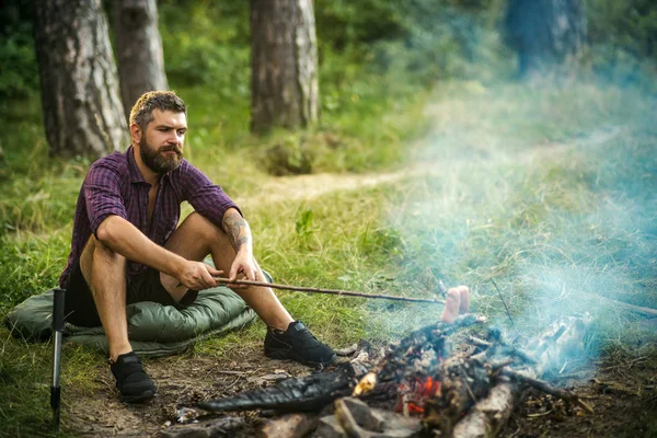 Homme randonneur rôti saucisses sur bâton sur le feu de joie dans la forêt — Photo