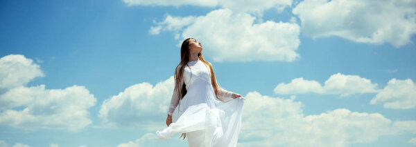 Girl or woman with long hair in white dress enjoy sunny summer day on cloudy blue sky. Freedom, future concept