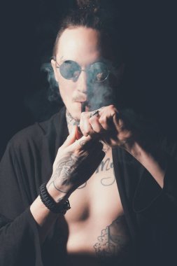 Adam sigara içen güneş gözlüğü ve dövmeli gövde gösterilen açık giyim
