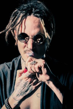 Adam yasaktır boru siyah arka plan üzerine dövmeli elinde. Güneş gözlüğü ve çıplak göğüs dreadlocks ile hippi sigara içen. Kötü alışkanlık, bağımlılık. Sağlıksız yaşam tarzı kavramı. Konsantrasyon, stres.