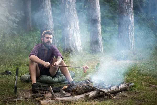 Hombre viajero asado salchichas en palo en fogata en el bosque —  Fotos de Stock