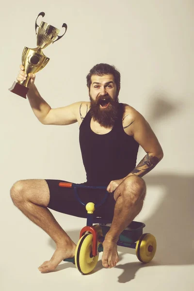 Homem feliz barbudo detém copo campeão de ouro no brinquedo de bicicleta — Fotografia de Stock