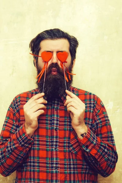 Funny bearded man håller röda hjärtan på pinnar inför ögon — Stockfoto