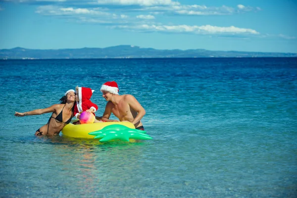 Weihnachtsfamilie mit Weihnachtsmütze am Strand mit Matratze — Stockfoto