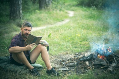 Adam gezgin okumak ve kamp ateşi alev içki