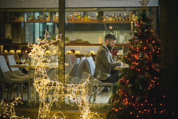 Man hipster sit at Christmas tree in restaurant