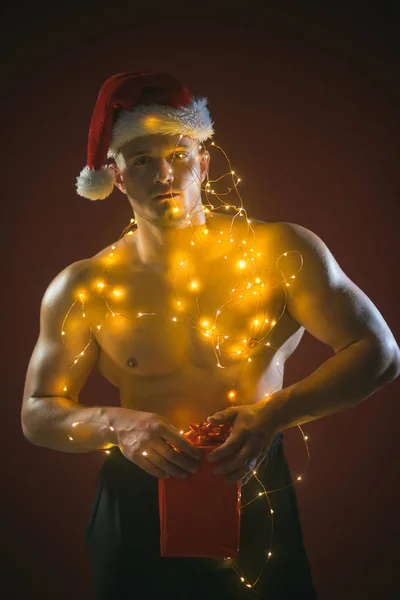 ガーランドで筋肉ボディを持つサンタ クリスマス パーティーとセックス ゲーム クリスマスでセクシーなアスリートの男性や少年を呼び出します サンタ衣装の若い男は 女の子のため提示します 新年のストリップ 大人向けのギフト — ストック写真
