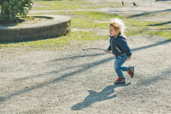 Feliz niño en chaqueta azul y pantalones vaqueros con palo — Foto de Stock