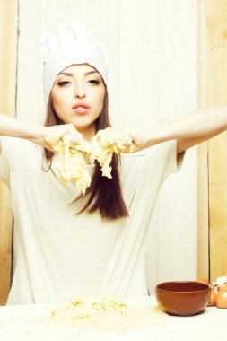 Bir güzel genç kadın aşçı yemek hamur un elinde ve mutfak ahşap zemin, dikey resim üzerine yumurta ile ev yapımı yemek önlük ve şapka profesyonel beyaz üniformalı