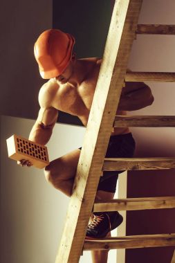 genç yakışıklı maço adam Oluşturucu ile seksi kaslı atletik güçlü vücut çıplak gövde ve güçlü karın altı paketleri ile ya da turuncu baret veya kask abs tuğla Ahşap merdiven üzerinde tutar.