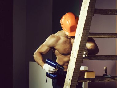 genç yakışıklı maço adam Oluşturucu ile seksi kaslı atletik güçlü vücut çıplak gövde ve güçlü karın altı paketleri ile ya da tuğla ve yumruk Ahşap merdiven yakınındaki abs turuncu baret veya kask tutar