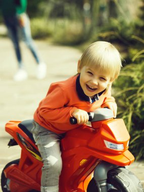 Yüz ve plastik oyuncak Bisiklet Park el ele tutuşarak ailesiyle oturan sarışın gülümseyen mutlu küçük çocuk arka plan bulanık