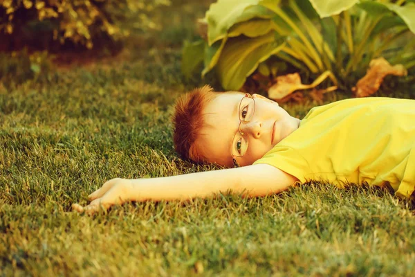 Happy baby boy z rude włosy w okularach na trawie — Zdjęcie stockowe