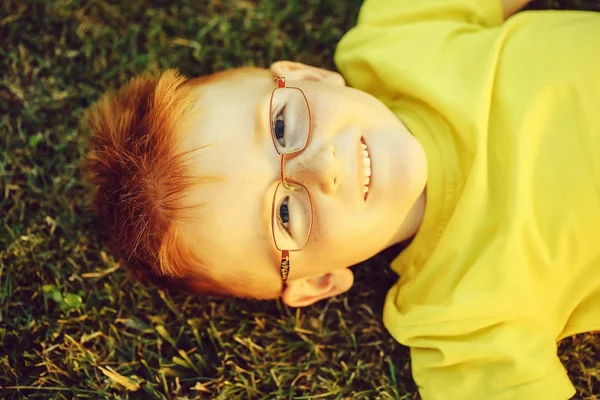 Menino feliz com cabelo vermelho em óculos na grama — Fotografia de Stock