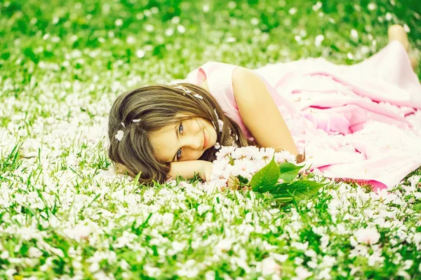 Liten flicka på grönt gräs med kronblad — Stockfoto