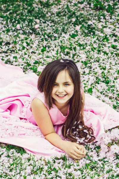 Kleines Mädchen auf grünem Gras mit Blütenblättern — Stockfoto