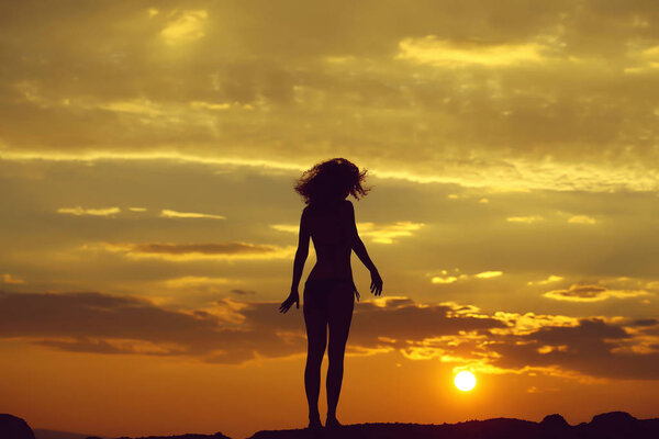 Young woman silhouette on beach near sea or ocean water in evening or twilight sunset summer day on natural background