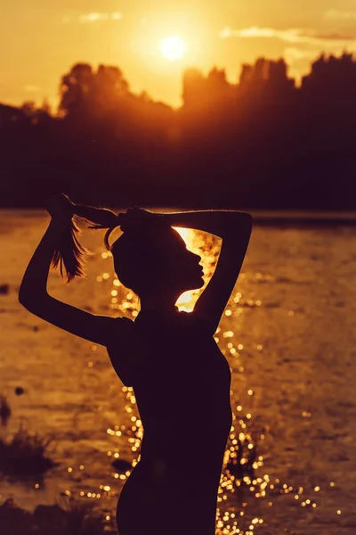 female silhouette near water on sunset