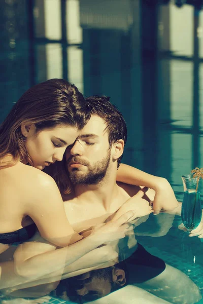 muscular man and sexy woman in blue pool with cocktail