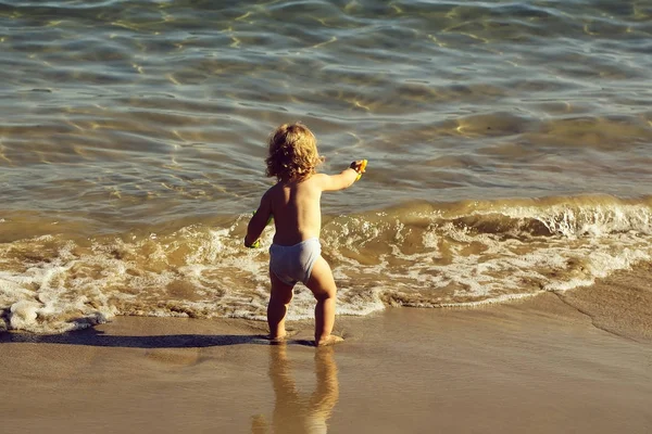 金发碧眼的小孩子好奇男孩站在海海岸海滩与波浪水阳光黄昏户外玩在自然背景下 水平图片 — 图库照片