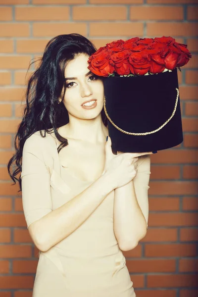Ganska nöjd flicka leende med röda rosor i låda — Stockfoto