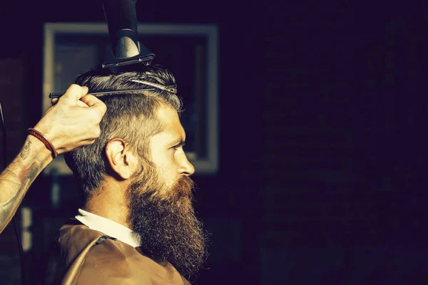 Bearded man getting hair styling by hairdresser at barbershop