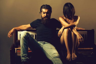 Uzun sakallı yakışıklı bir adam ciddi bir yüzle genç bir kadın ya da kızın yanında üstsüz seksi göğüsleri ya da göğüsleri çıplak vücudu ve külodu eski ahşap piyano klavyesinin yanında.