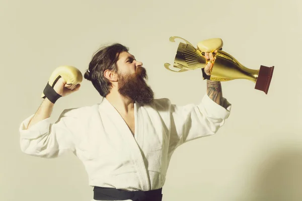 bearded happy karate man in kimono, boxing gloves, champion cup