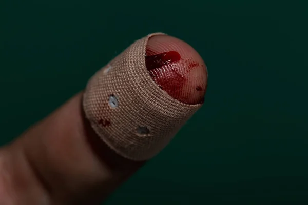 Finger with red blood and plaster on green background — Stock Photo, Image