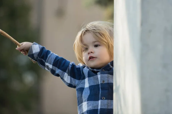 Kind met blond haar in blauwe geruite shirt met stok — Stockfoto